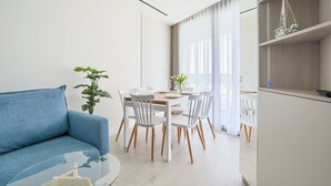 A modern living room with a blue sofa, a dining table set for four, and a kitchen area with a wooden cabinet and a hanging sailboat decoration. - Prywatne Apartamenty Sun & Snow w Wave (Miedzyzdroje)