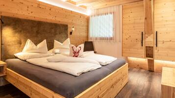 Ein schlicht eingerichtetes Schlafzimmer im Chalet-Stil mit Bett, Kissen, Kopfteil, Nachttisch, einem Fenster mit Vorhängen und einem Holzschrank.