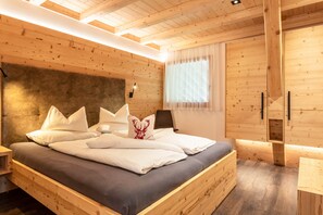 Ein schlicht eingerichtetes Schlafzimmer im Chalet-Stil mit Bett, Kissen, Kopfteil, Nachttisch, einem Fenster mit Vorhängen und einem Holzschrank.