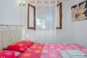 A bedroom with a bed, a window with a curtain, a wall lamp, and a painting.