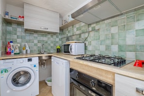 A compact kitchen with a washing machine, microwave, gas stove, and a small sink.