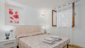 Une chambre à coucher comprenant un lit, une table de chevet, une lampe, une œuvre d’art accrochée au mur et une fenêtre avec un rideau.