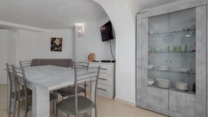 Un coin repas comprenant une table en marbre, des chaises en métal, un téléviseur fixé au mur et une vitrine contenant de la vaisselle.