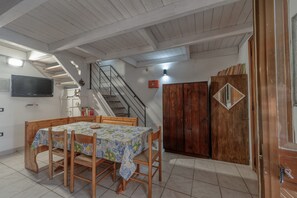 A dining area with a table and chairs, a staircase, wooden cabinets, and a television on the wall.