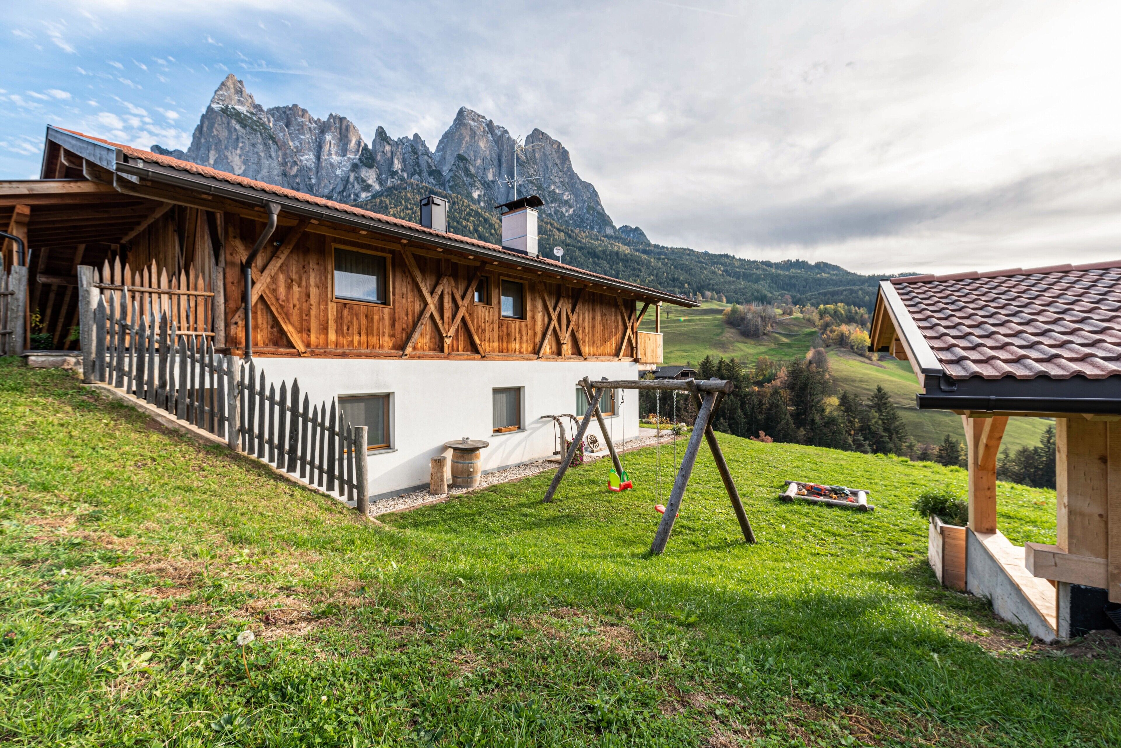 A wooden chalet with a sloped roof, a wooden fence, and a swing set.
