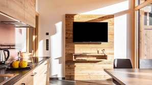 A modern kitchen with a wooden wall, a flat-screen TV, and a dining area with a table and chairs. - Holiday Apartment "Zu Grof Morgenrot" (Castelrotto)