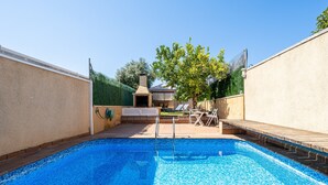 Una piscina amb una zona de solàrium escalonat, una zona de barbacoa i un arbre al fons.