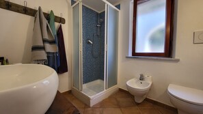 Un baño con una bañera blanca grande, una ducha con mosaicos azules, un lavamanos blanco y un inodoro.