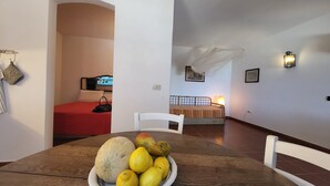 A room with a bed, a dining table with fruit, a chair, and a TV in the background. - Strandhaus 'Perla di Mare' direkt am Meer (Capoliveri)