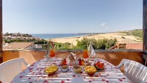 Una mesa con comida y bebidas en un balcón con vista a una playa.
