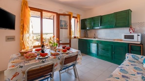 Un comedor con una mesa dispuesta para dos, una cocina con armarios verdes y un televisor montado en la pared.
