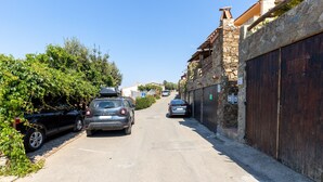 Una calle estrecha con coches aparcados, edificios de piedra y un cielo azul despejado.