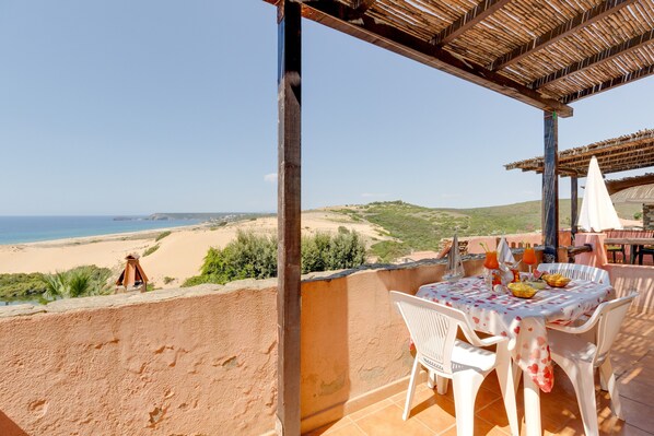 A terrace with a table set for dining, overlooking a beach and hills.
