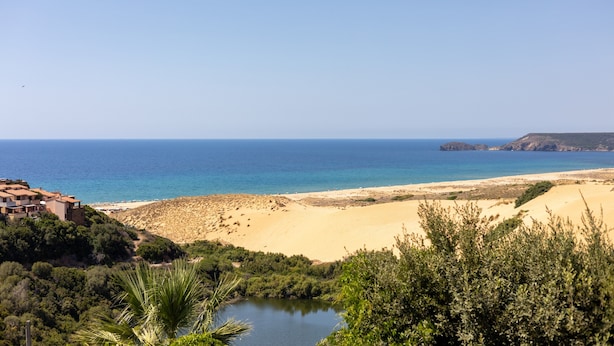 Un paisaje costero con una playa, una masa de agua y un edificio con techo inclinado.