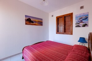 A bedroom with a bed, a window, and two wall-mounted paintings.