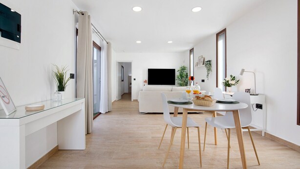 A modern living space with a dining area, a sofa, a TV, and a desk with a lamp. - Holiday Apartment "Crepusculo" with Mountain View, Terrace & Wi-Fi (Puerto del Rosario)