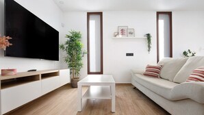 A modern living room with a flat-screen TV, a white coffee table, a sofa with striped cushions, a potted plant, and a wooden floor. - Holiday Apartment "Crepusculo" with Mountain View, Terrace & Wi-Fi (Puerto del Rosario)