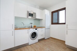 Eine moderne Küche mit weißen Schränken, einer Edelstahl-Mikrowelle, einer Waschmaschine und einem Fenster mit braunem Rahmen.