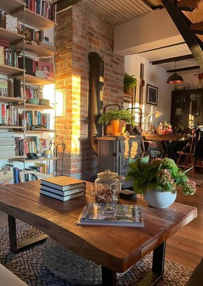 A cozy living room with a brick fireplace, a wooden coffee table, bookshelves, and a dining area. - Beautiful Wooden Cottage in Nature, Croatia (Velika Gorica)