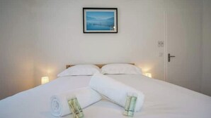 A neatly made bed with white linens and rolled towels, a framed picture on the wall, and a door with a handle. - The Family Lake - Appartement 2 Chambre, Terrasse & Parking (Lathuile)