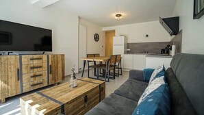 A modern living room with a sofa, coffee table, and wooden cabinets. There is a dining area with chairs and a table, and a kitchen area with a refrigerator and sink. - The Family Lake - Appartement 2 Chambre, Terrasse & Parking (Lathuile)
