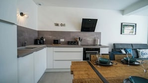 A modern kitchen with white cabinets, a wooden countertop, and a built-in oven. There is a dining table with chairs and a sofa in the adjacent living area. - The Family Lake - Appartement 2 Chambre, Terrasse & Parking (Lathuile)