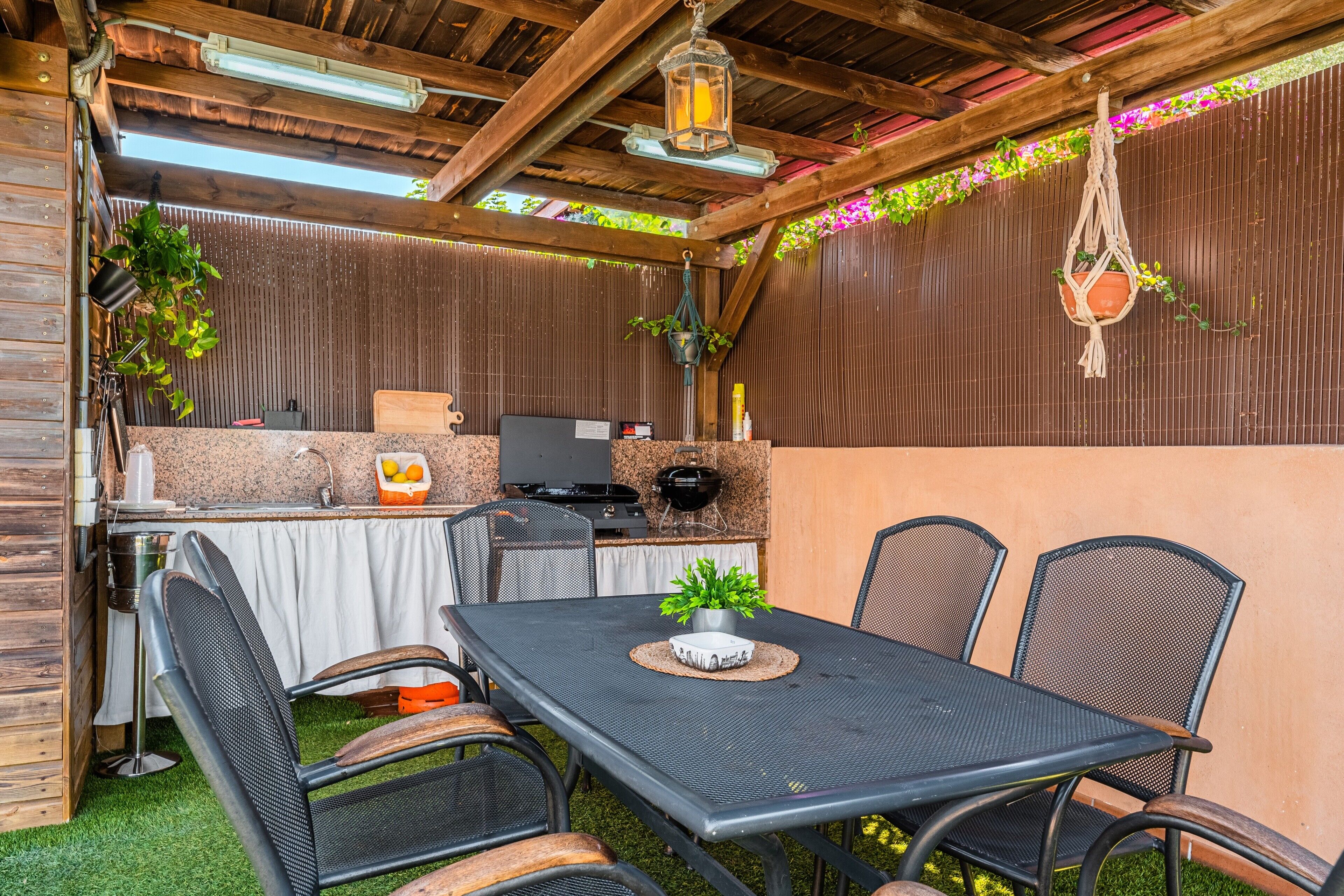 Een terras buiten met een tafel, stoelen, een barbecue en hangplanten.
