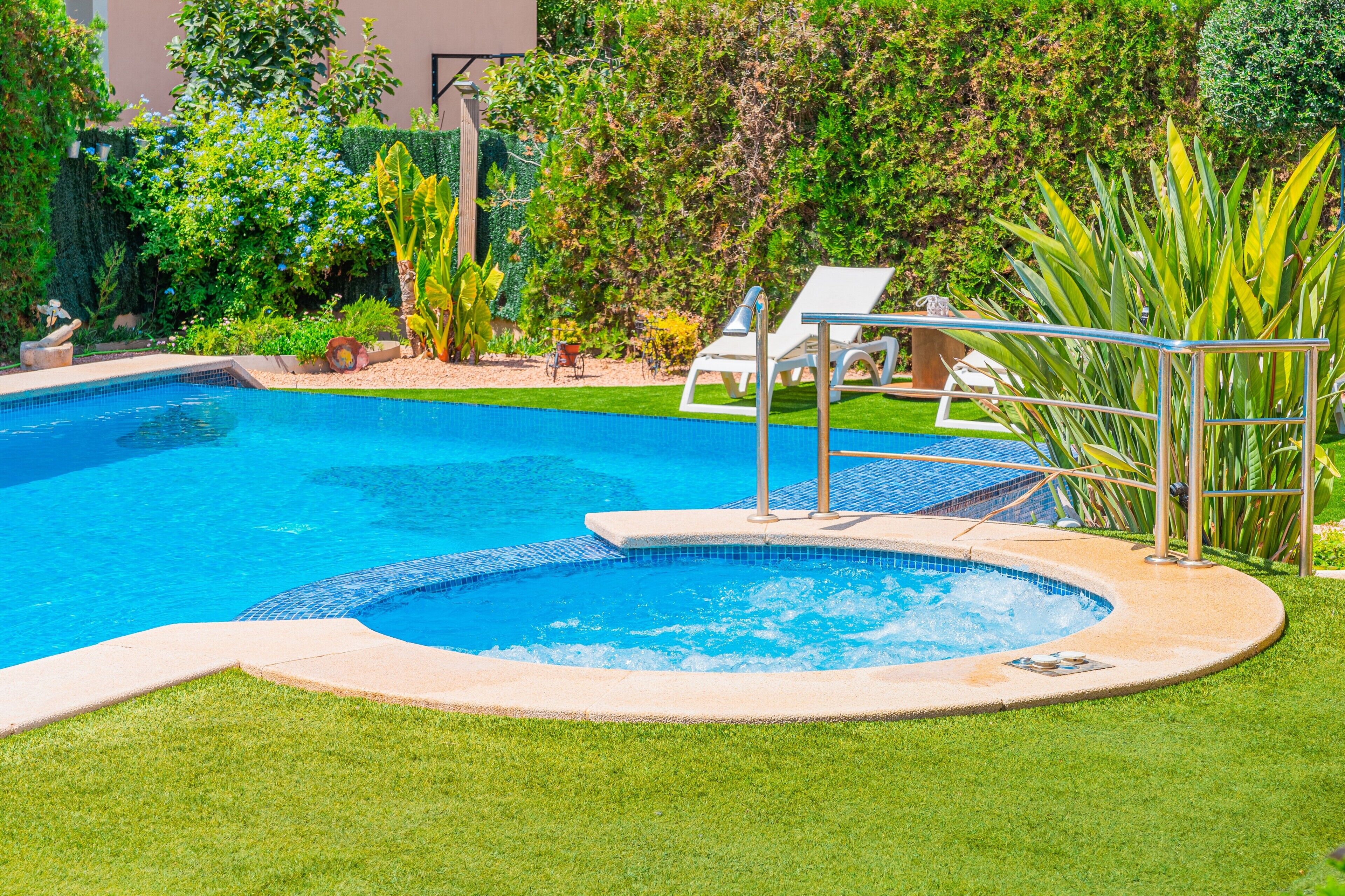 A swimming pool with a hot tub, surrounded by grass and plants.