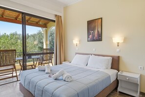 A hotel room with a bed, a nightstand, a table with chairs, and a view of greenery outside.