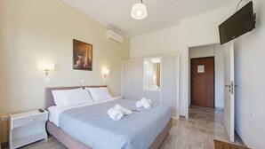 A hotel room with a bed, bedside tables, a TV, and a door leading to another room.