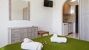 A room with a bed, a wooden dresser, a television, and a kitchen area visible through an archway. - Studio Apartment 'Alexandra Studio 11' with Private Balcony and Wi-Fi (Lefkimmi)