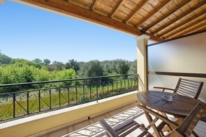 En balkon med træloft, et bord med stole og udsigt til grønne omgivelser.