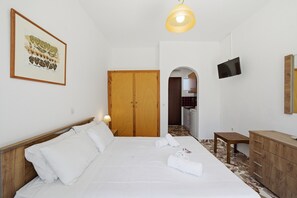 A bedroom with a bed, a wooden wardrobe, a television, and a framed picture on the wall.
