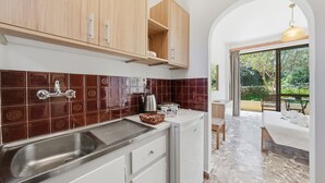 Een keuken met een spoelbak, kastjes en een aanrecht met een waterkoker en kopjes.