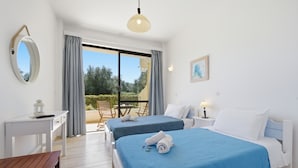 A hotel room with two beds, a desk, a chair, a table, and a view of the outdoors.