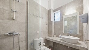 Un baño moderno con cabina de ducha de cristal, inodoro, lavabo con espejo y secador de pelo montado en la pared.