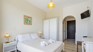 Un dormitorio con cama, lámparas de noche, escritorio, televisor y una puerta que da a otra habitación.