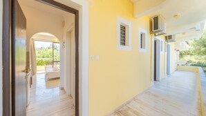 Un pasillo con piso de madera, pared amarilla y una puerta que da a una habitación con cama y ventana.