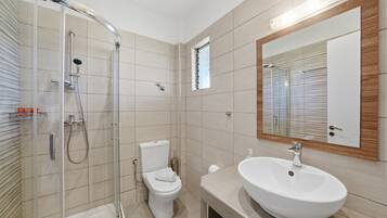 Un bagno moderno con cabina doccia in vetro, un water, un lavandino e uno specchio.