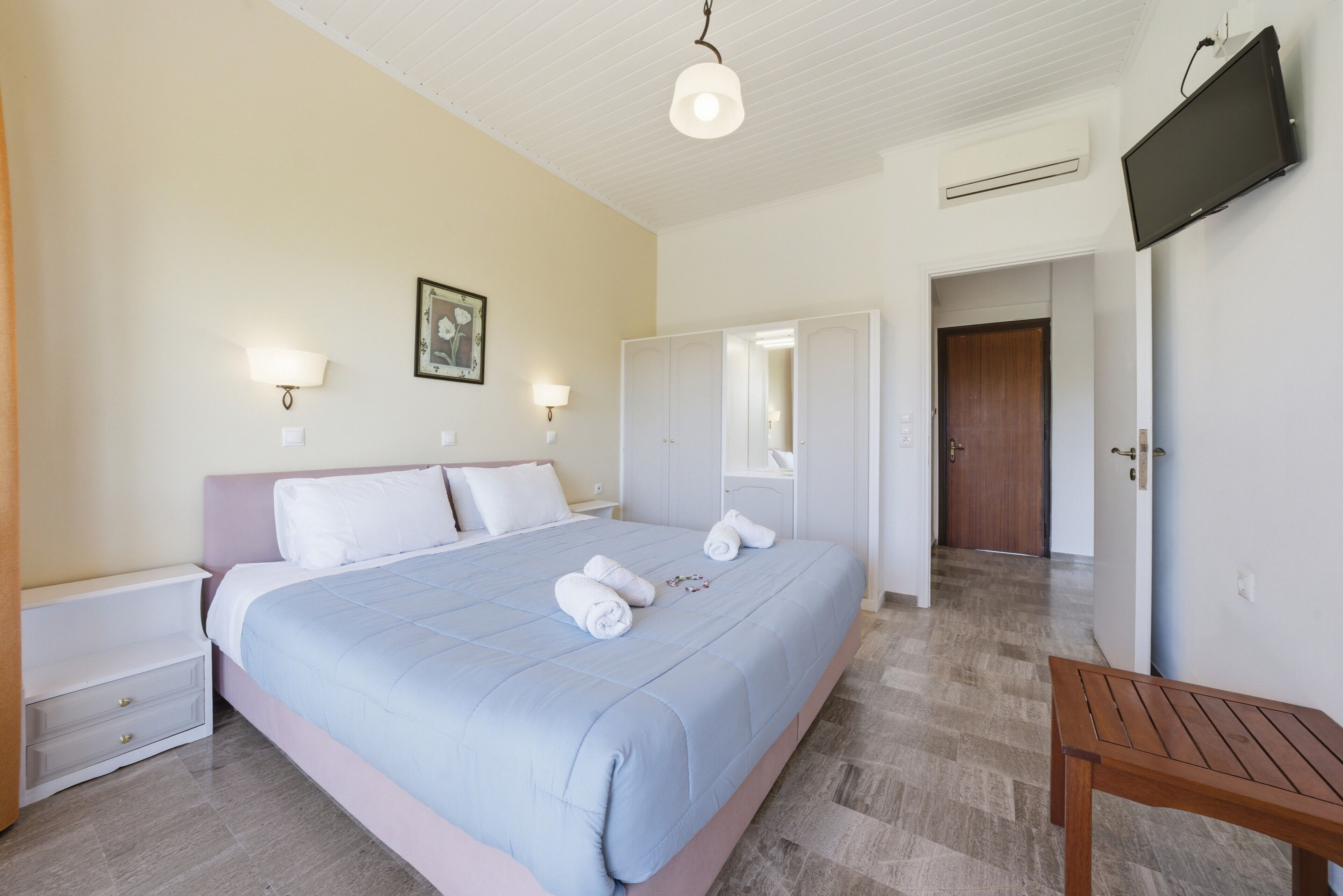 Una camera da letto con un letto, comodini, una panca in legno, una televisione e un armadio.