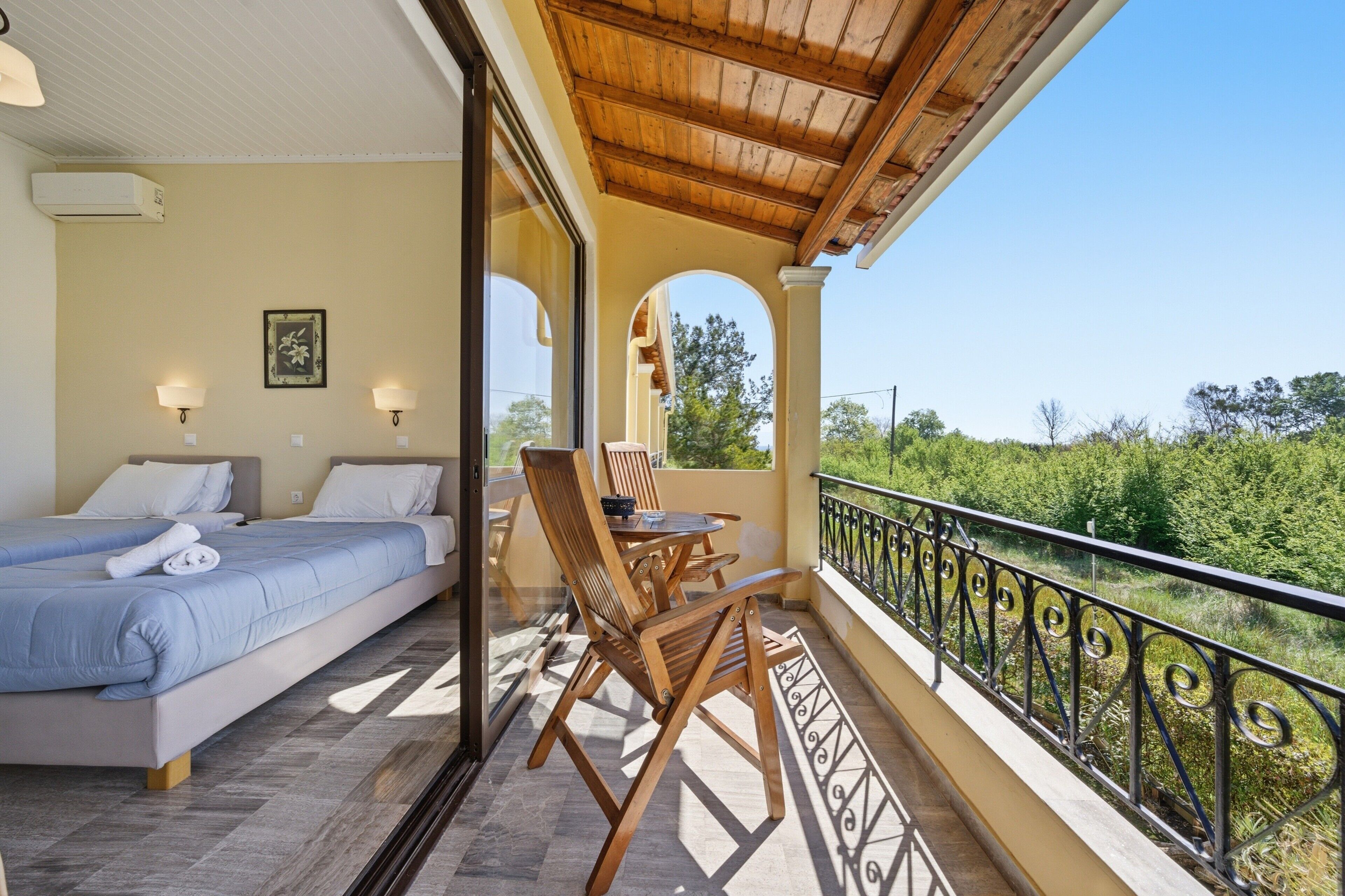 Una camera da letto con due letti, un balcone con tavolo e sedie, e vista sul verde.