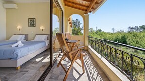 Ein Schlafzimmer mit zwei Betten, einem Balkon mit Tisch und Stühlen und Blick auf Grünflächen.