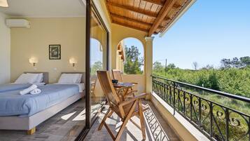 Una camera da letto con due letti, un balcone con tavolo e sedie, e vista sul verde.