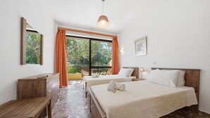 A hotel room with two beds, a wooden desk, a bench, a large window with curtains, and a hanging light fixture. - Studio Apartment 'Alexandra Studio 7' with Private Balcony & Wi-Fi (Lefkimmi)