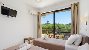 Een hotelkamer met twee bedden, een televisie, airconditioning, een balkon met een tafel en stoelen, en uitzicht op groen.