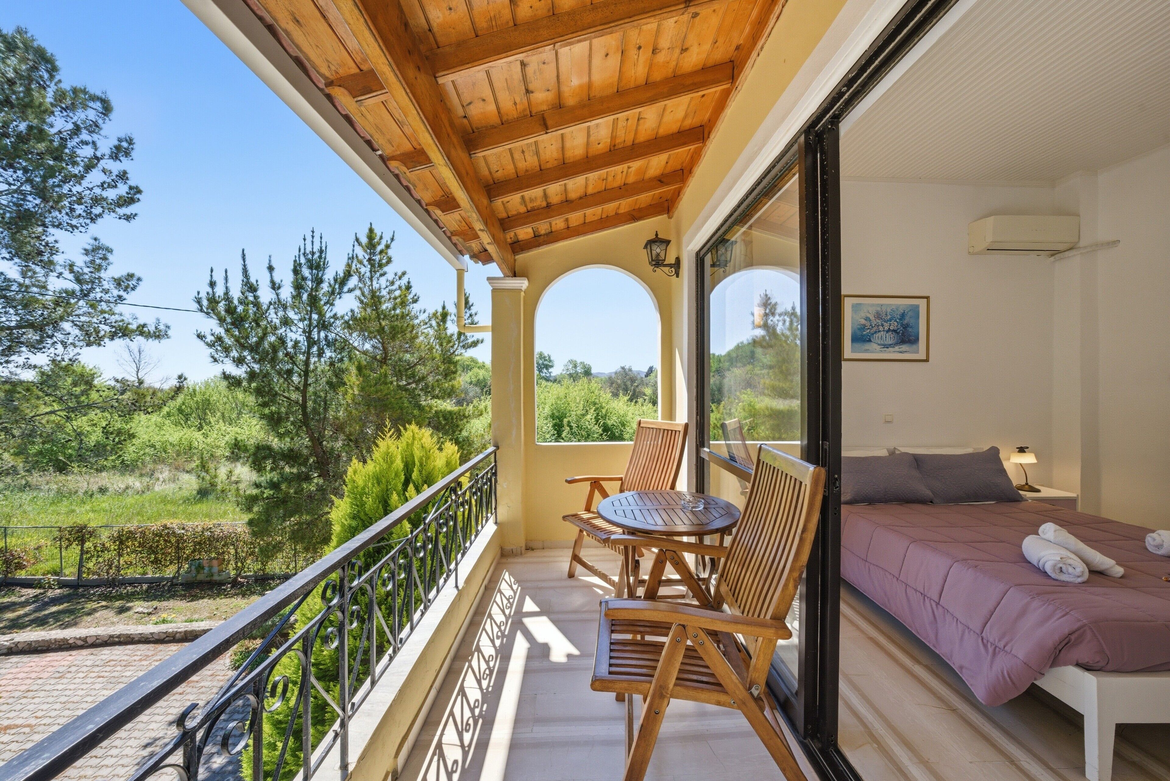 Un balcone con mobili in legno, un letto con copriletto viola e vista sul verde.