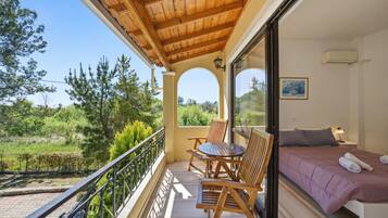 Un balcone con mobili in legno, un letto con copriletto viola e vista sul verde.