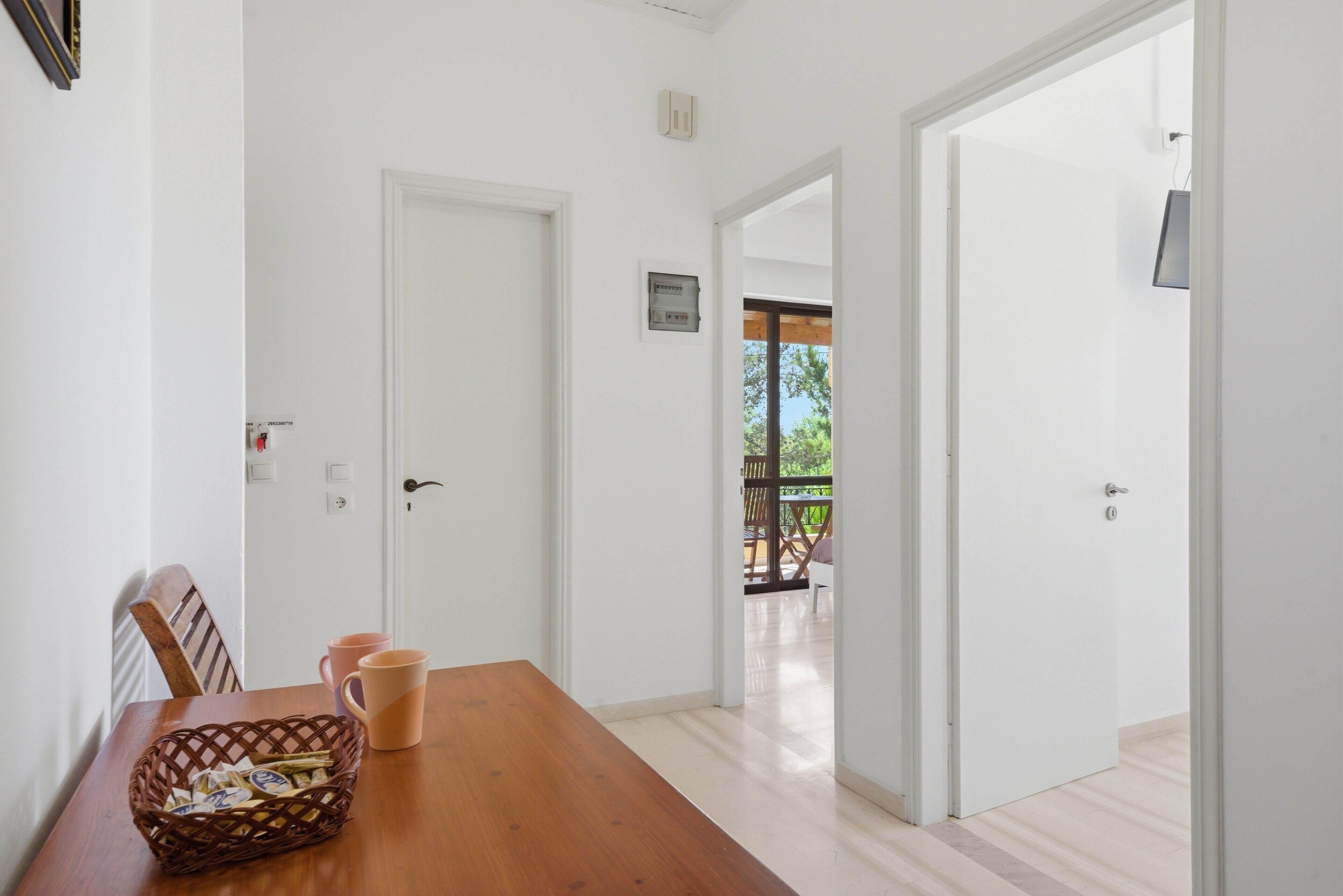 Una stanza con un tavolo da pranzo in legno, sedie, un cesto e una porta bianca che dà su uno spazio esterno.