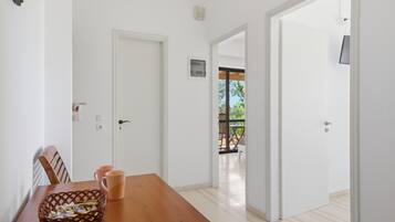 Una stanza con un tavolo da pranzo in legno, sedie, un cesto e una porta bianca che dà su uno spazio esterno.