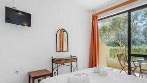 Une chambre d’hôtel avec un lit, un bureau, un miroir, une télévision et une vue sur la verdure.